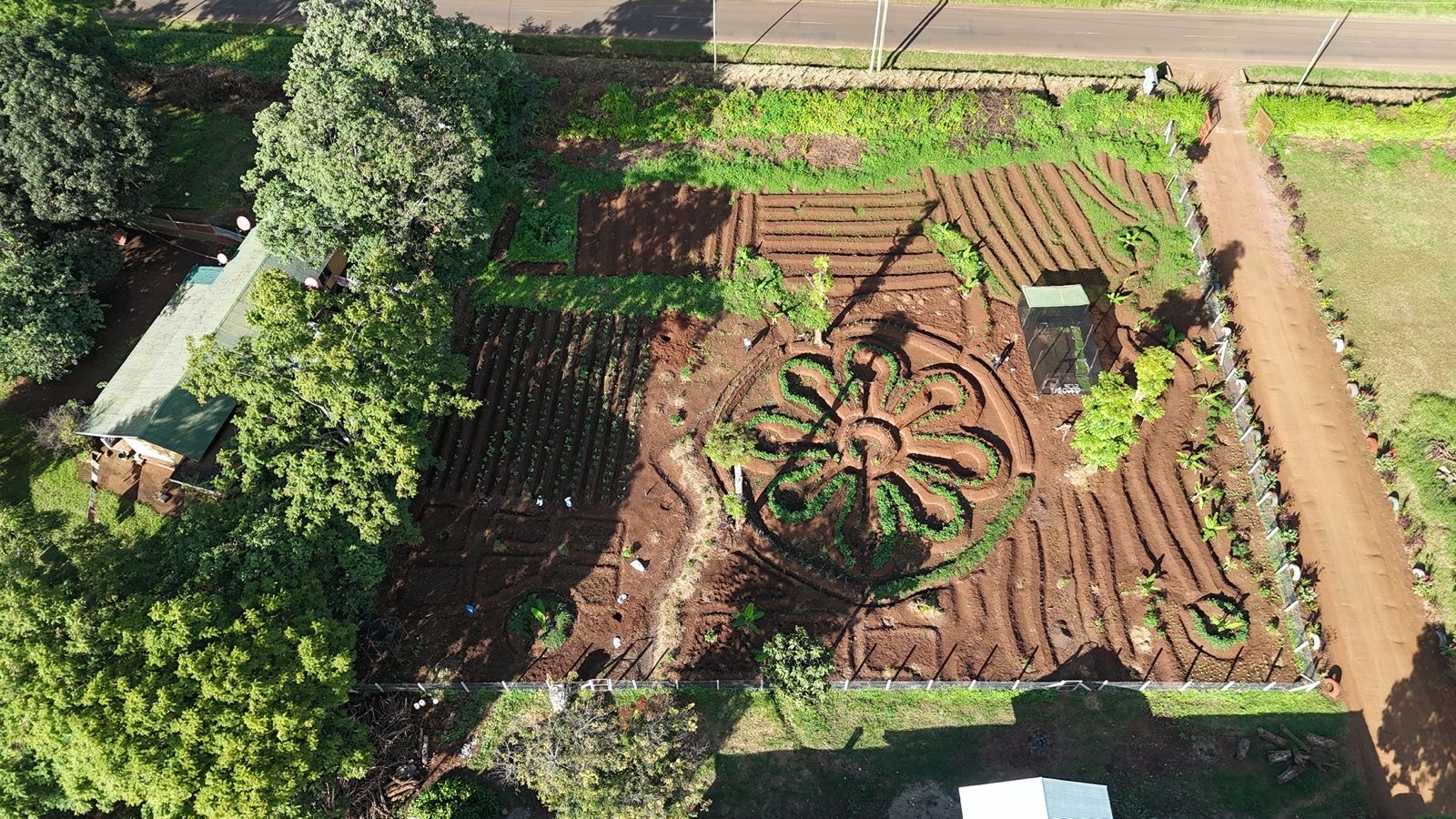 A second aerial angle of the same permaculture garden, showing its layout beside a school building and road